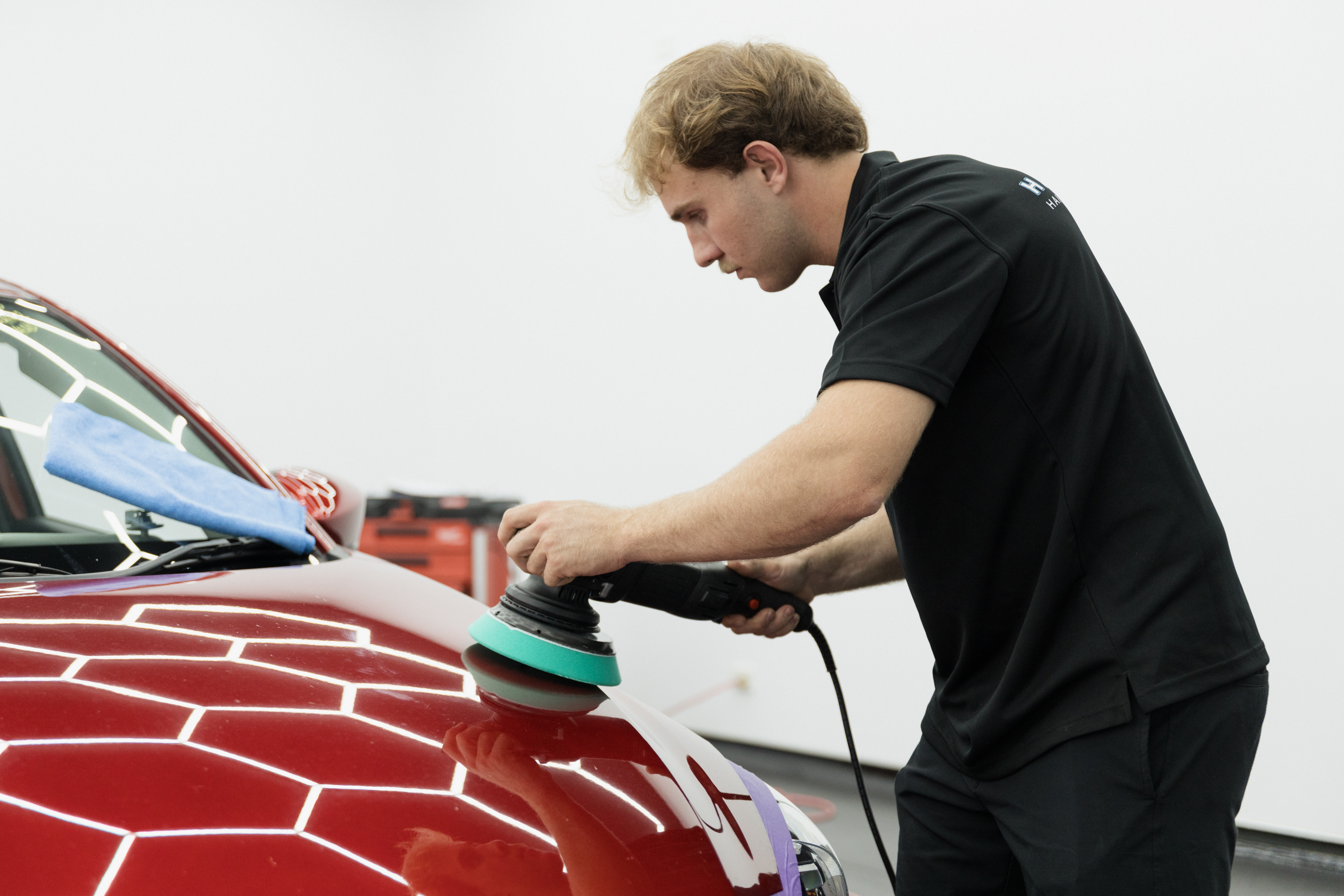 HS Autobody technician polishing a deep red car bonnet