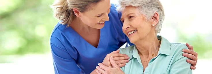 Carer assisting elderly woman in wheelchair outdoors