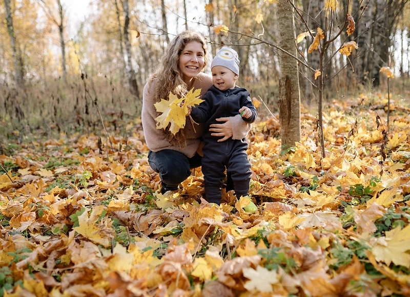 A part-time nanny playing with two children on a sunlit lawn outside a mountain home