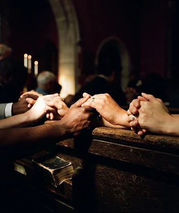 Hands clasped in prayer on a wooden pew