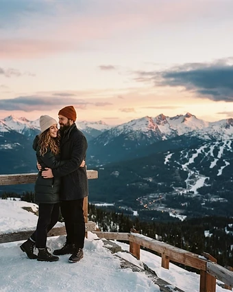A couple sharing a quiet moment on a snowy Whistler alpine viewpoint at sunset