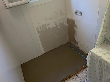 Salle de bain avant travaux — douche démontée, sol et murs bruts