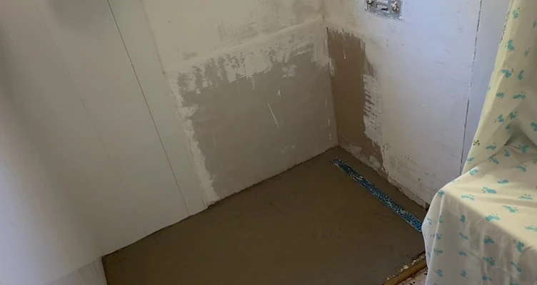 Salle de bain avant travaux — douche démontée, sol et murs bruts