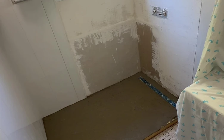 Salle de bain avant travaux — douche démontée, sol et murs bruts
