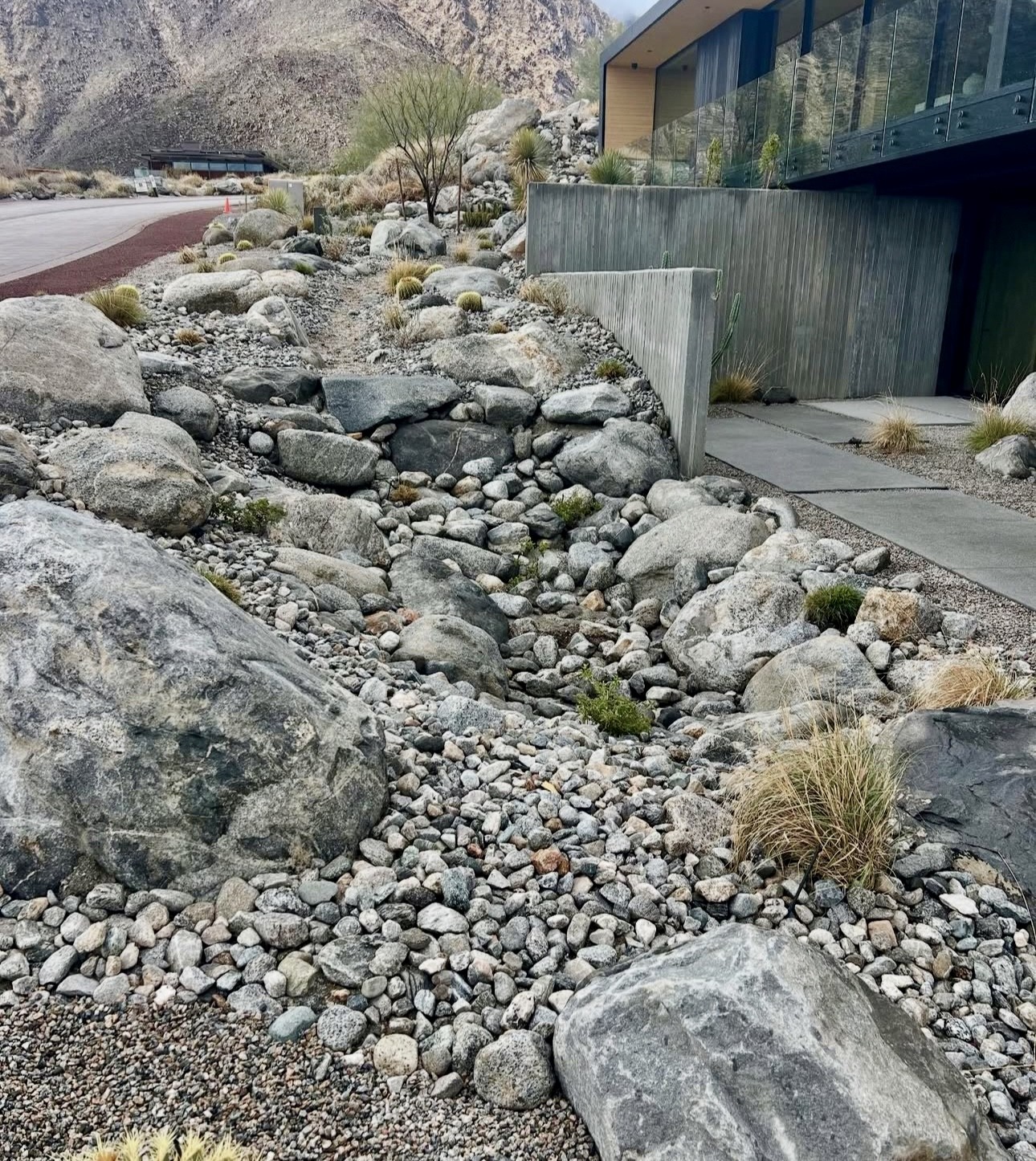 Arroyo drainage feature of rounded boulders beside a board-formed concrete wall.
