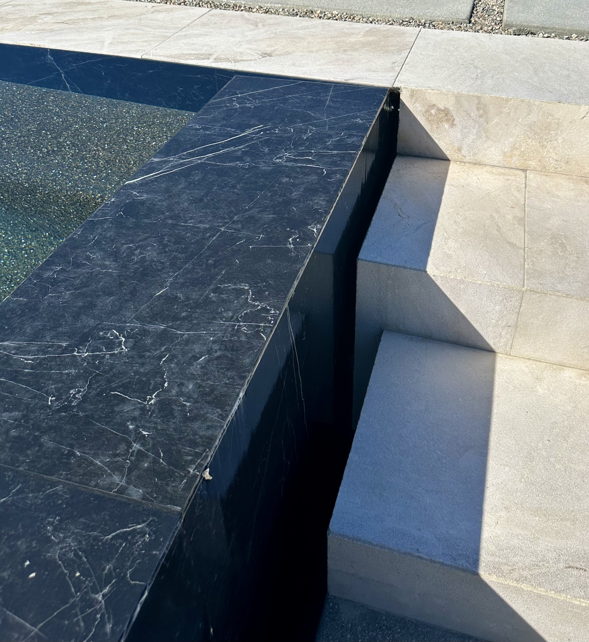 Detail of a dark polished pool edge meeting light stone steps.
