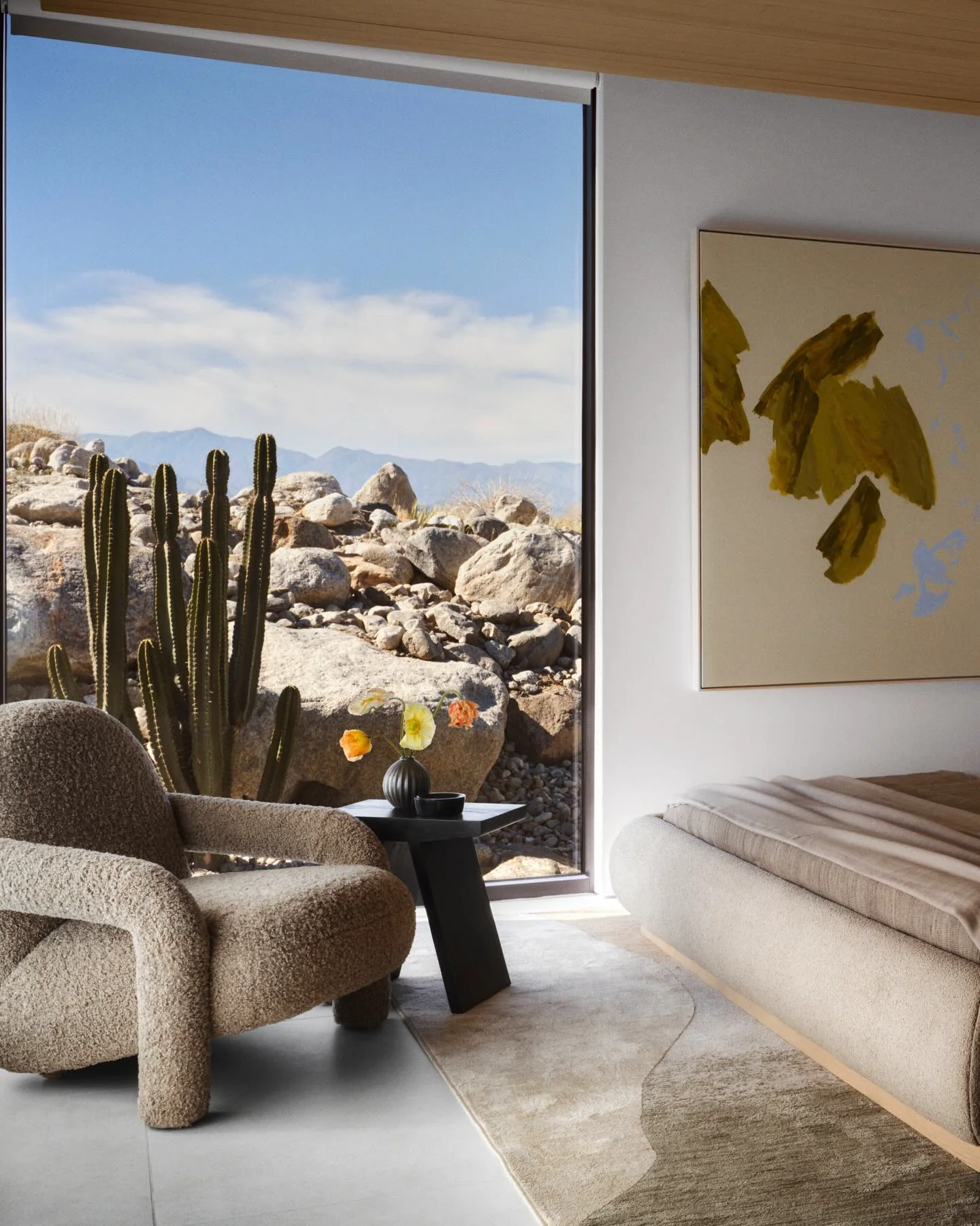 Bedroom opening toward a boulder garden, columnar cacti, and distant desert mountains.