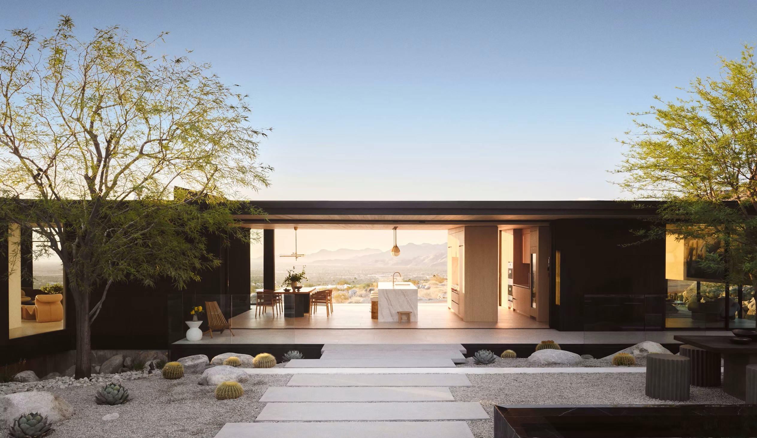 Courtyard axis extending through the open house toward a distant mountain range at golden hour.