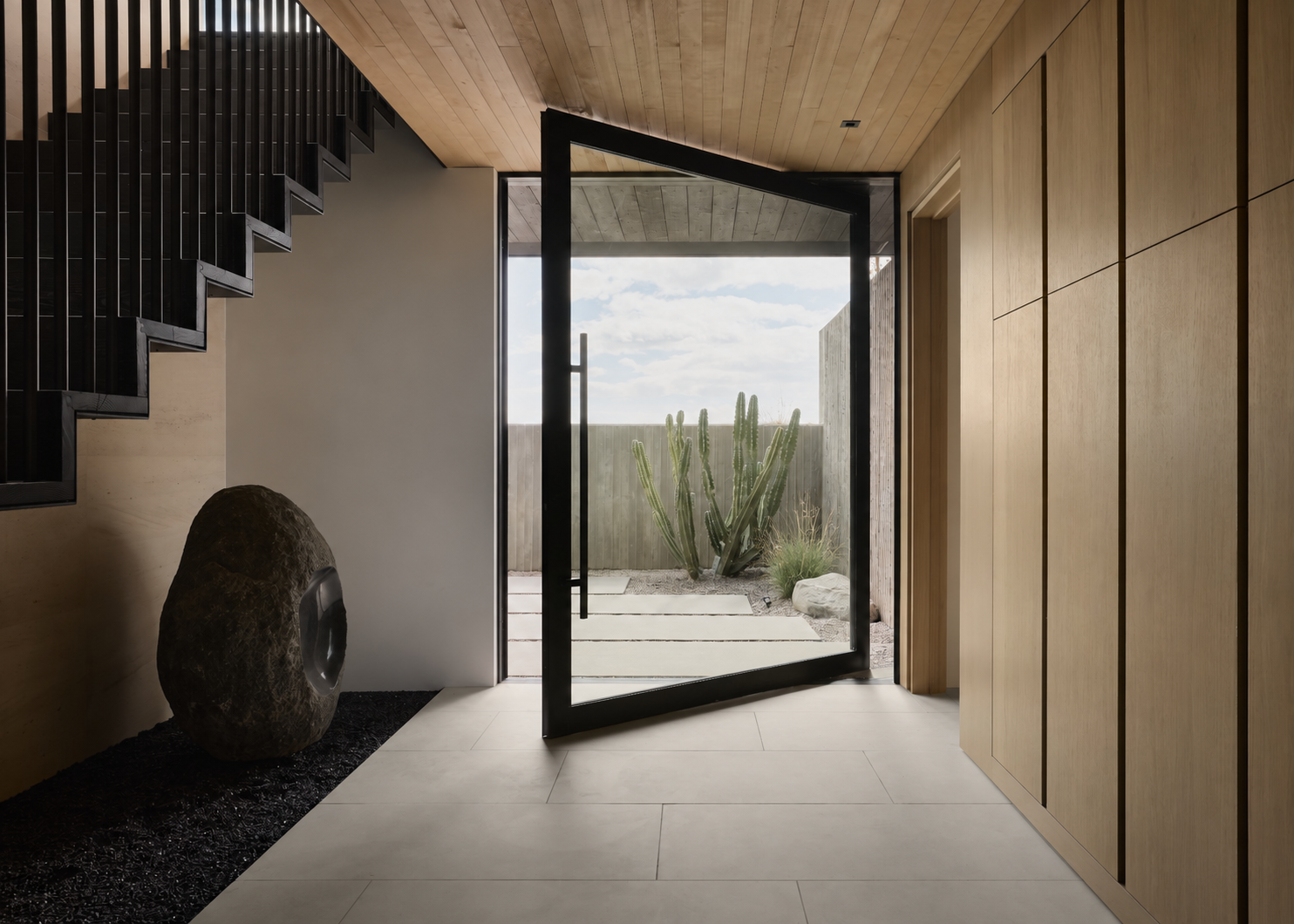Entry-hall pivot door opening to a desert garden with concrete stepping stones and a cactus.