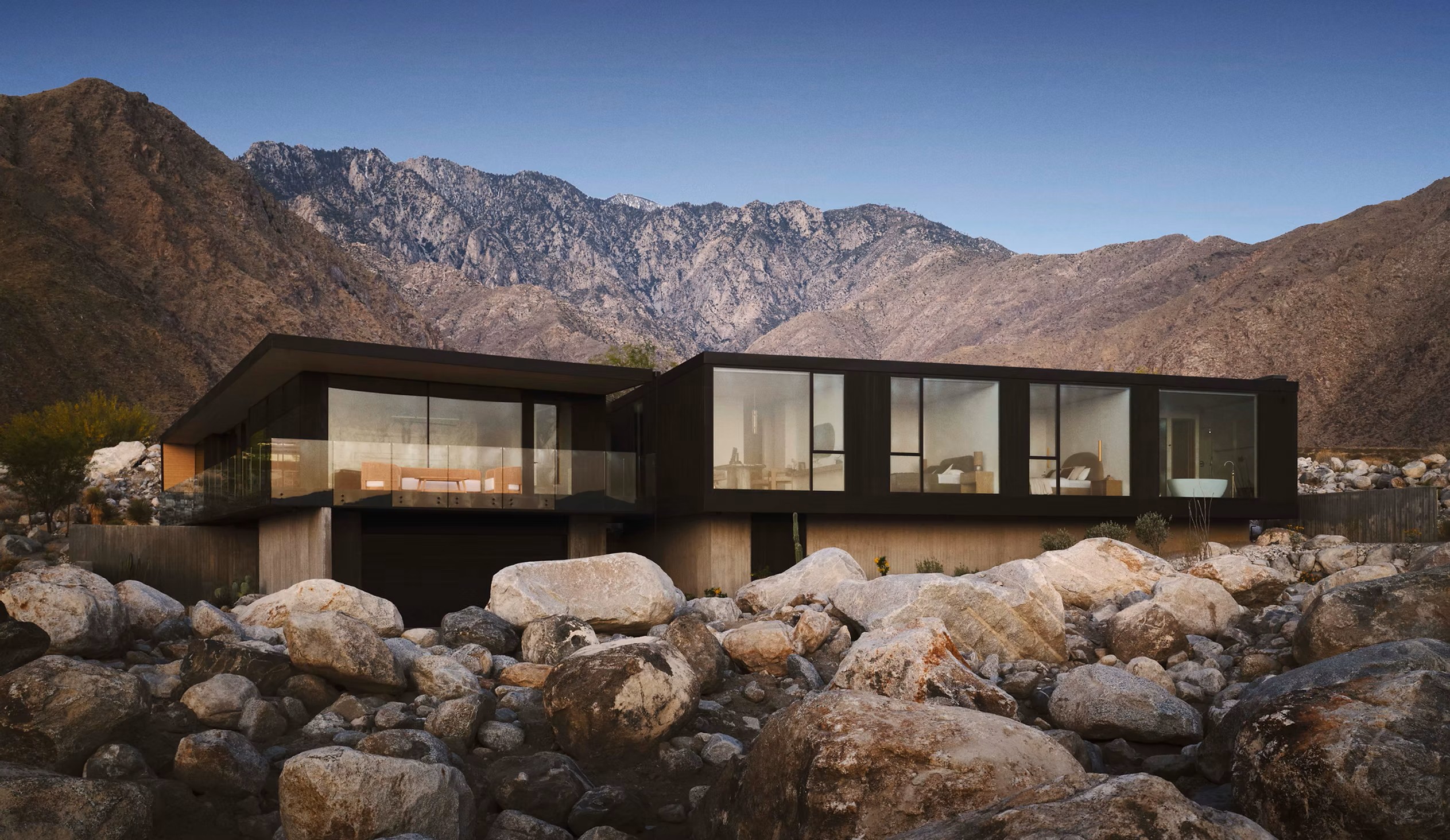 Wabi-Sabi House and boulder garden at dusk, backed by a mountain range under a deep blue sky.