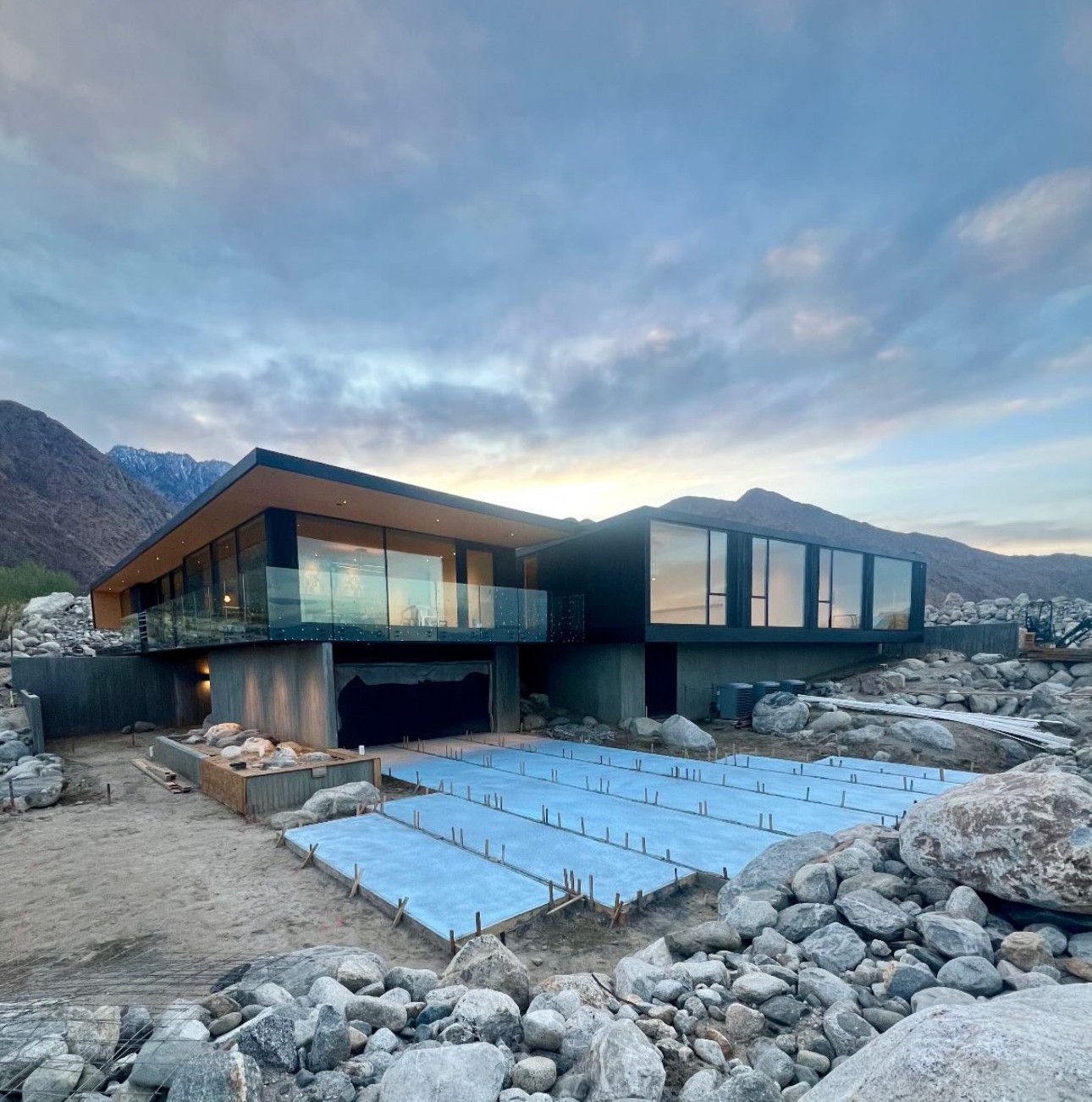 Wabi-Sabi House site under construction at dusk with boulders and concrete pads.