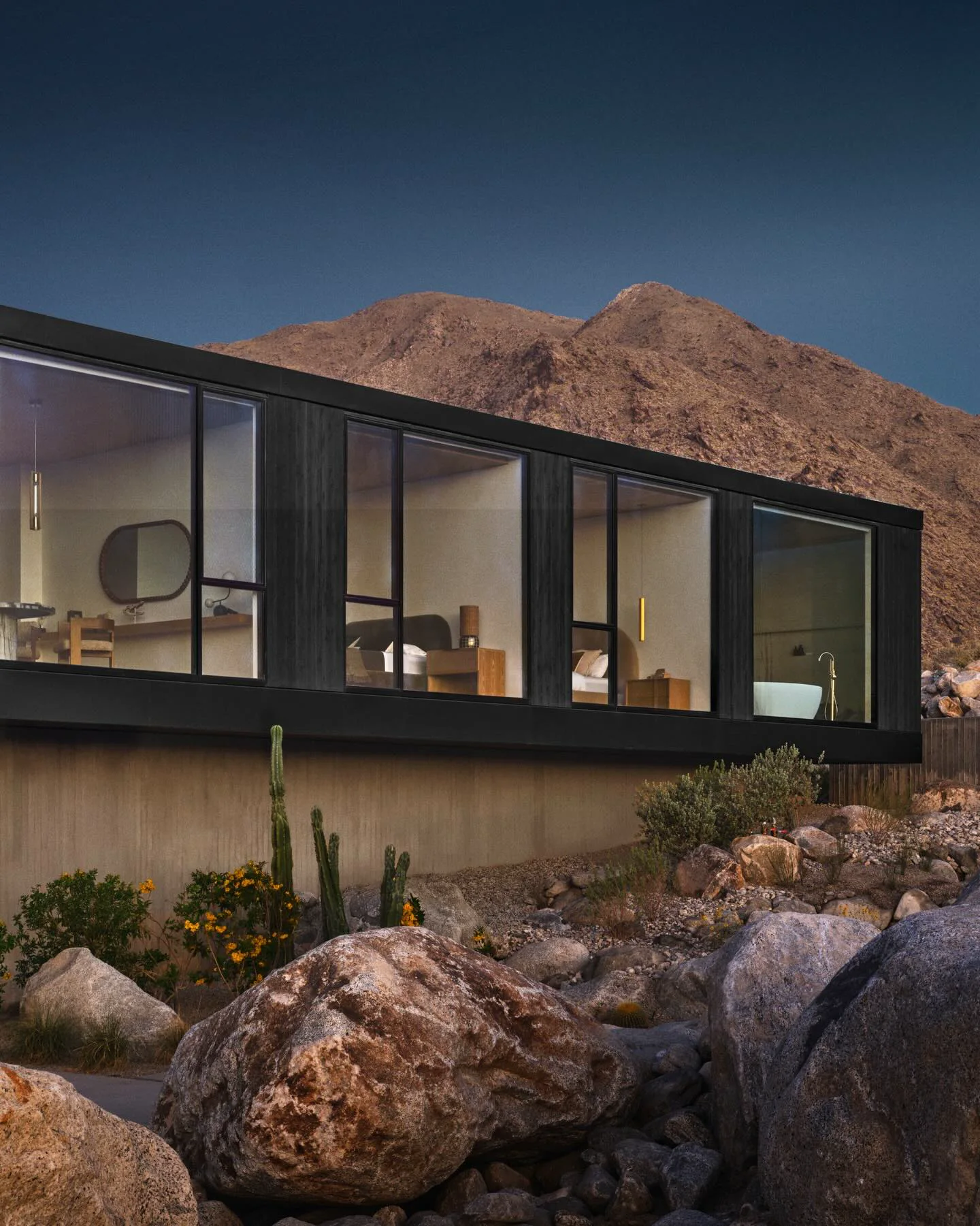 Desert residence framed by native boulders, cacti, and a mountain at dusk.