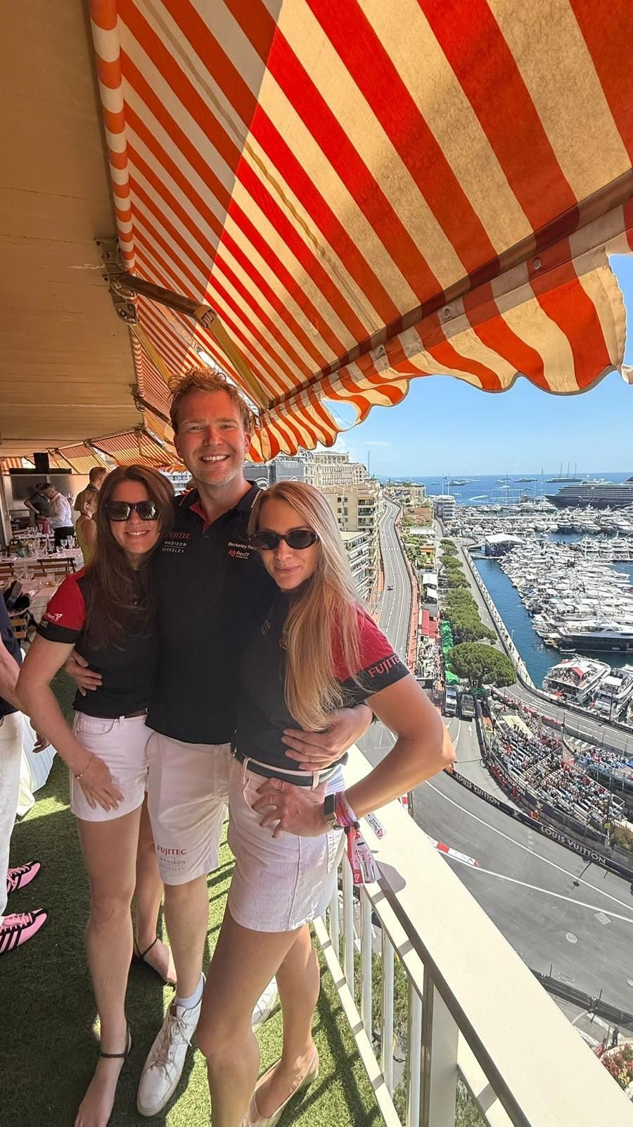 Three Berkeley Red hosts smiling on a terrace overlooking the Monaco harbour and circuit