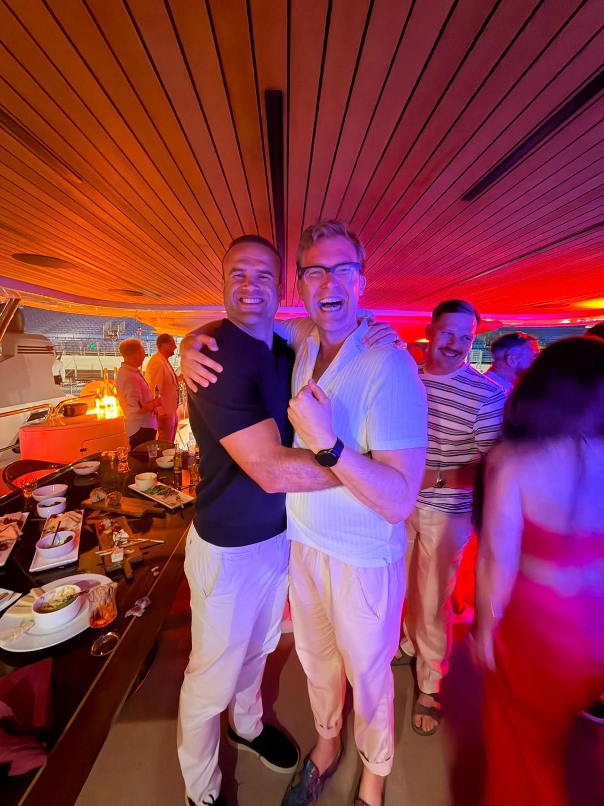 Guests embracing and laughing at a warm-lit dinner during a Monaco hospitality evening