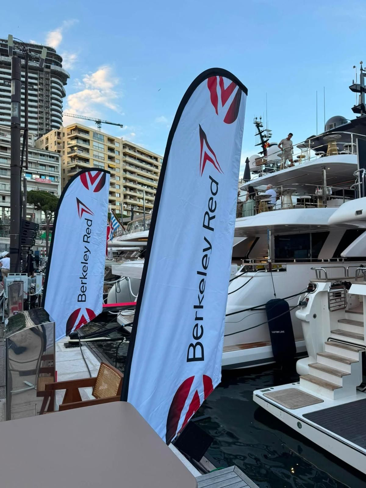 Berkeley Red feather flags beside a superyacht docked in Monaco harbour