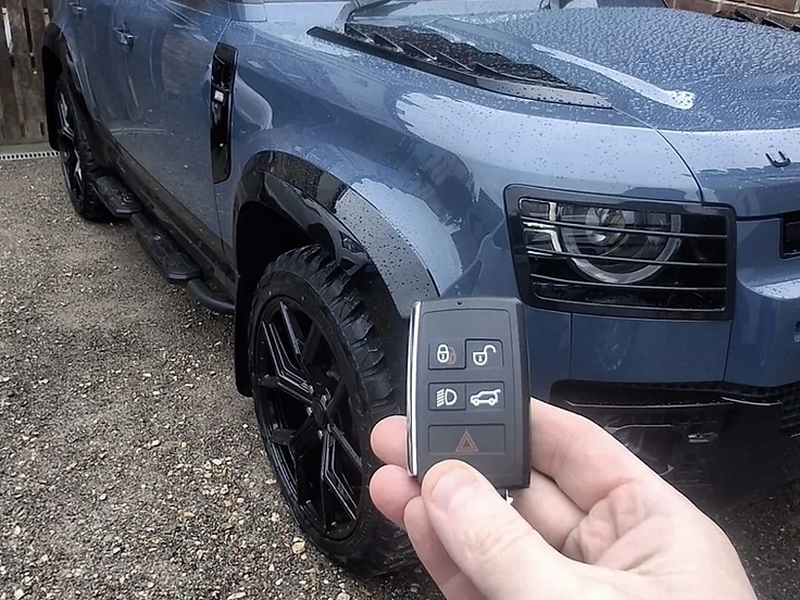 Freshly programmed Land Rover Defender smart key held in front of the customer's vehicle on a Cheshire driveway