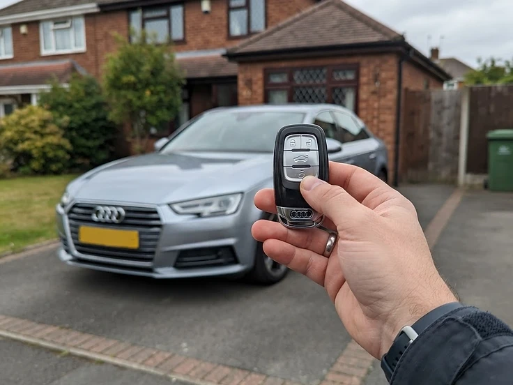 Audi key fob held in front of an Audi A4 on a driveway