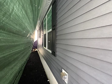 Green tarp secured along the side of a grey vinyl sided home