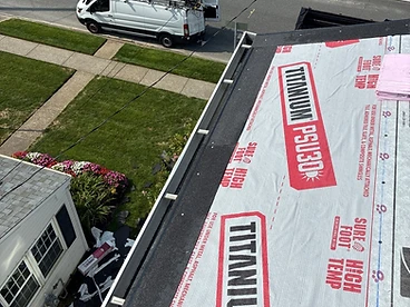 Hand pointing toward a black starter strip laid along the eave edge of a roof covered in grey TITANIUM PSU30 underlayment with a gutter below