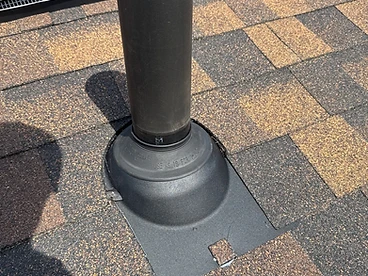 Close-up of a black rubber Oatey pipe boot flashing collar sealed around a black PVC vent pipe on architectural shingles with sealant at the collar and flange