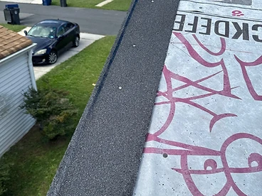 Dark grey asphalt starter strip fastened along the edge of a roof deck covered in light grey Owens Corning Deck Defense underlayment with magenta paw print branding