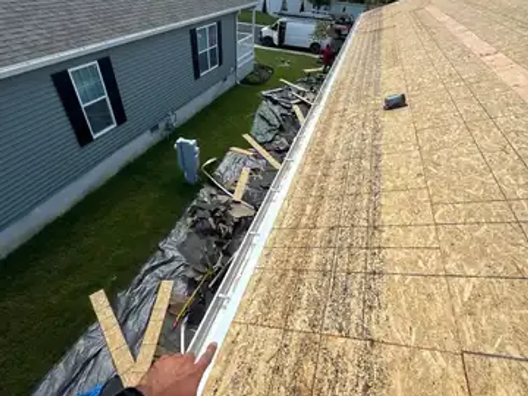Hand pointing at a white metal drip edge strip running along the eaves of a roof with exposed OSB sheathing