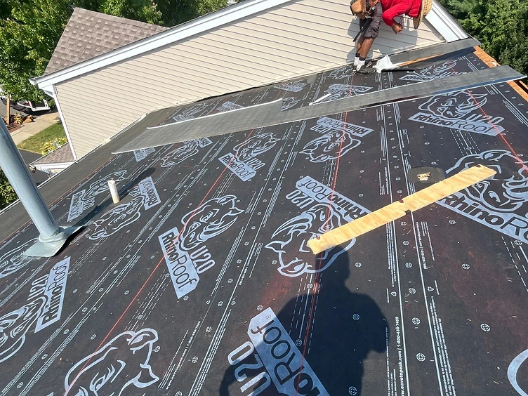 First-person view down a pitched roof covered in black RhinoRoof U20 synthetic underlayment installed in overlapping horizontal courses with red alignment lines
