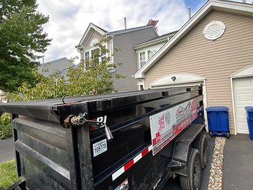 Black 15 cubic yard Veterans Roofing debris trailer with mesh tarp and branding parked on a residential driveway