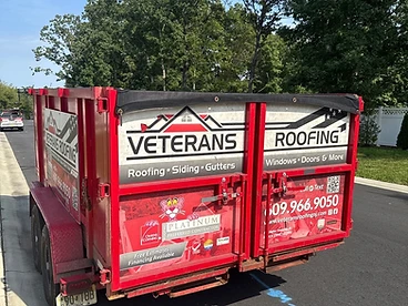 Rear quarter view of a red Veterans Roofing debris trailer with branding, QR code, and Owens Corning Platinum Preferred badge on the rear doors