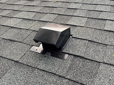 Black hooded roof ventilation cap installed on grey architectural shingles with the flange layered under shingles above and over shingles below and sealant at the junction