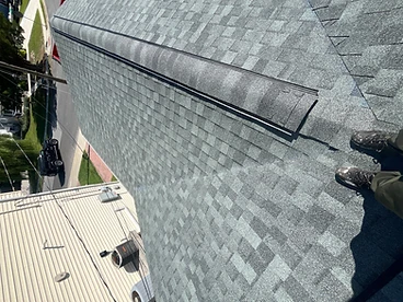 Top-down view of grey slate hip and ridge cap shingles installed along a hip line with a black ventilation strip visible beneath the overlapping caps