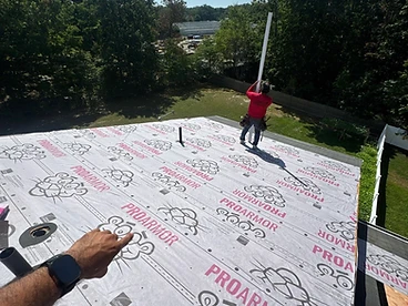 Light grey Owens Corning ProArmor synthetic underlayment with pink Pink Panther branding installed in horizontal courses with a worker holding a PVC pipe