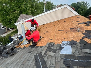 Elevated view of three workers on a partially stripped roof with exposed OSB sheathing and a metal chimney stack