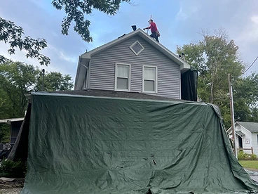 Two-story home with green tarp protecting the side wall during tear-off
