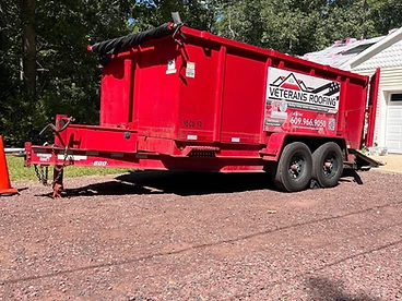 Red 15 cubic yard Veterans Roofing dump trailer viewed from the rear quarter on a gravel driveway with branding and contact info