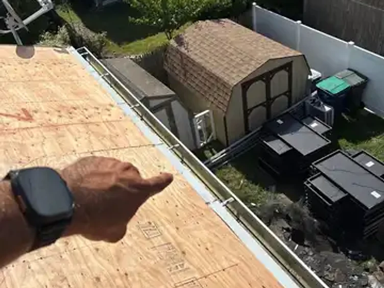 Hand pointing toward a newly installed metal gutter and drip edge flashing system along the roof edge with OSB decking