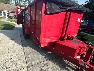 Red Veterans Roofing dump trailer with rear gate open and black mesh tarp system on a concrete driveway