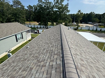 Completed grey and slate hip and ridge cap shingles installed in an overlapping staggered pattern along the peak of a gabled roof