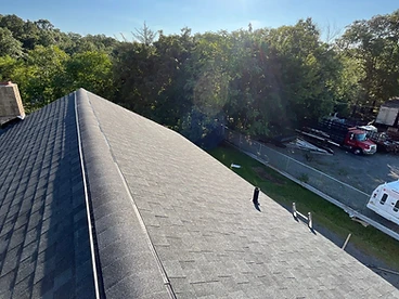 Charcoal hip and ridge cap shingles installed along the ridge of a dark grey architectural shingle roof with a chimney and vent pipe visible