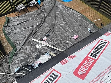 Hand pointing at a dark granular starter strip installed flush along the bottom edge of a roof deck covered in grey TITANIUM PSU30 synthetic underlayment