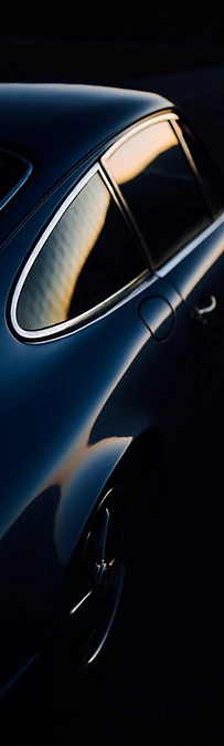 Close detail of a navy classic coupé at dusk, its glass and rear panel catching the last low light