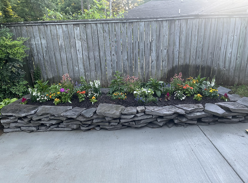 Dry-stack stone retaining wall with a colorful raised flower bed on a coastal property