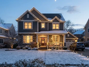 A home with neat warm white holiday lights along the rooflines at dusk.