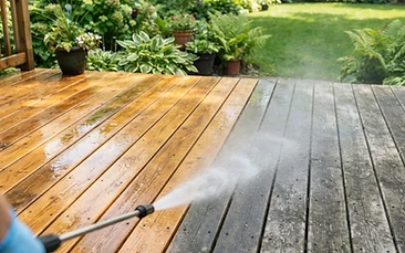 A wooden deck half washed clean and half still weathered grey, with fine spray in the air.