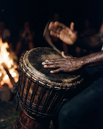 Hands mid-motion drumming a traditional African djembe, lit by warm amber firelight