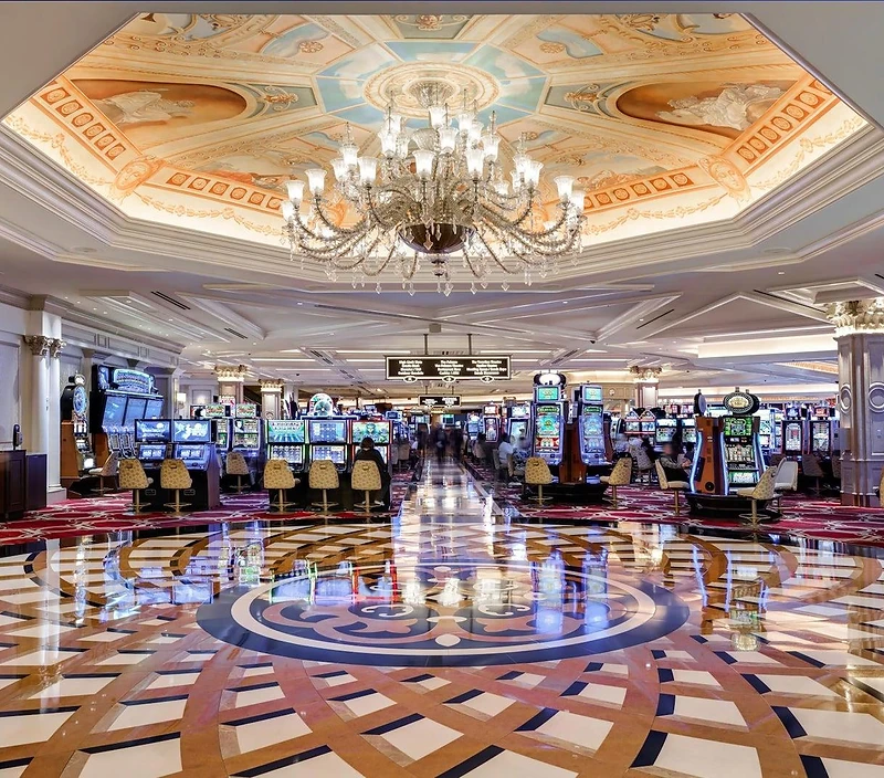 Interior of an upscale casino floor with an ornate coffered ceiling and crystal chandelier