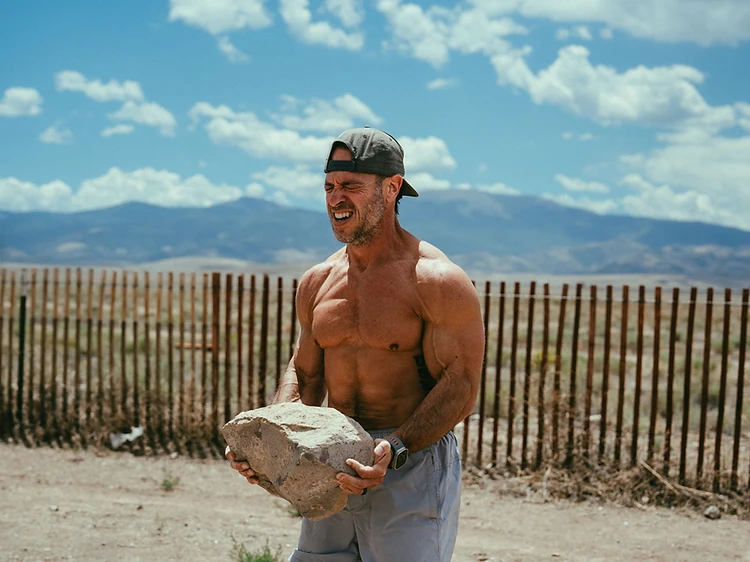 Muscular man holding a heavy rock outdoors