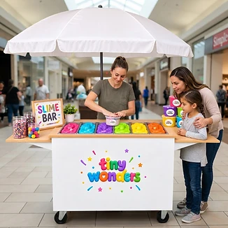Illustrative mall scene of an attendant packaging slime while a parent and child watch at the counter