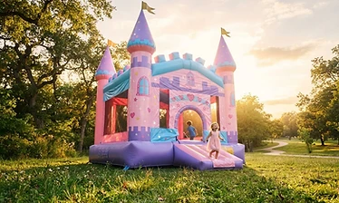 Fairytale castle themed inflatable bounce house in pastel colors in a sunny park