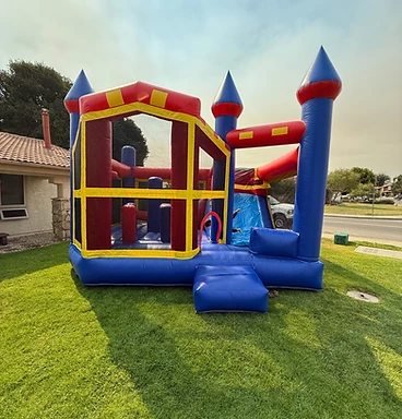 Castle Slide Combo bounce house with an attached blue slide in bold red, blue and yellow, set up on a Central Coast lawn